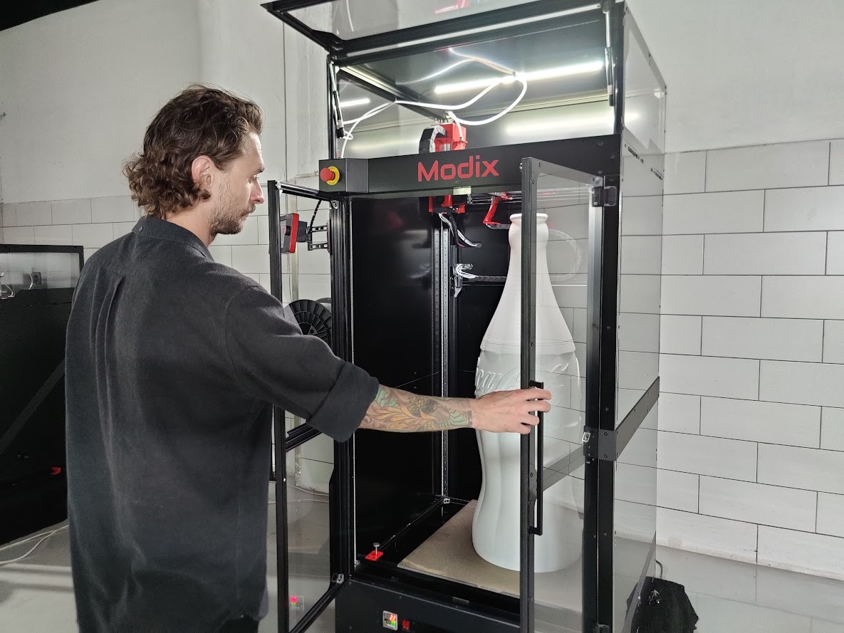 Opérateur devant une imprimante 3D Modix BIG-120Z contenant une grande pièce verticale imprimée en 3D